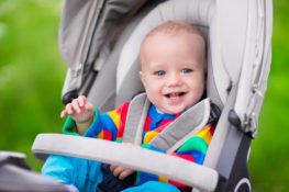 Baby boy in warm colorful knitted jacket sitting in modern stroller on a walk in a park