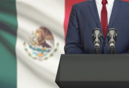 body of new mexican president at podium in front of mexico's flag