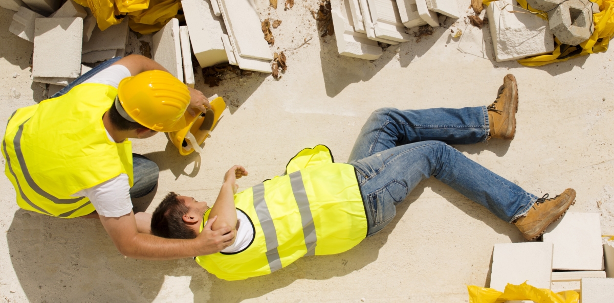 hurt construction worker laying on the floor and being assisted by a coworker