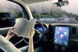 self-driving car with driver pictured reading a book
