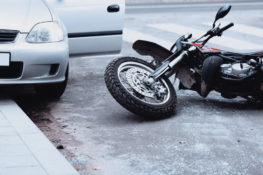 wrecked motorcycle hit by grey car parked on curb