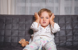 toddler boy holding ears sitting on couch with a teddy bear