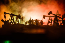 Oil war concept. Military silhouettes at oilfield with pumps and rigs. Misty colorful sky background. Armored vehicles fighting scene. Selective focus