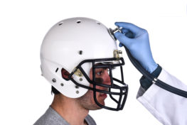 A football player wearing a helmet with doctors hand holding a stethoscope on the crown of the helmet. Sports Concussion Concept, and related conditions, CTE, Alzheimer's, Parkinson's
