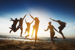 group of friends jumping in air on beach sunset
