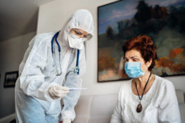 nurse with protection suit assisting elderly woman at a nursing home